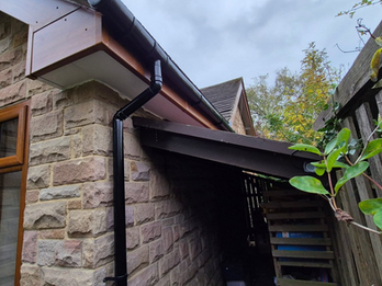 Newly installed black guttering along the roofline of a stone property