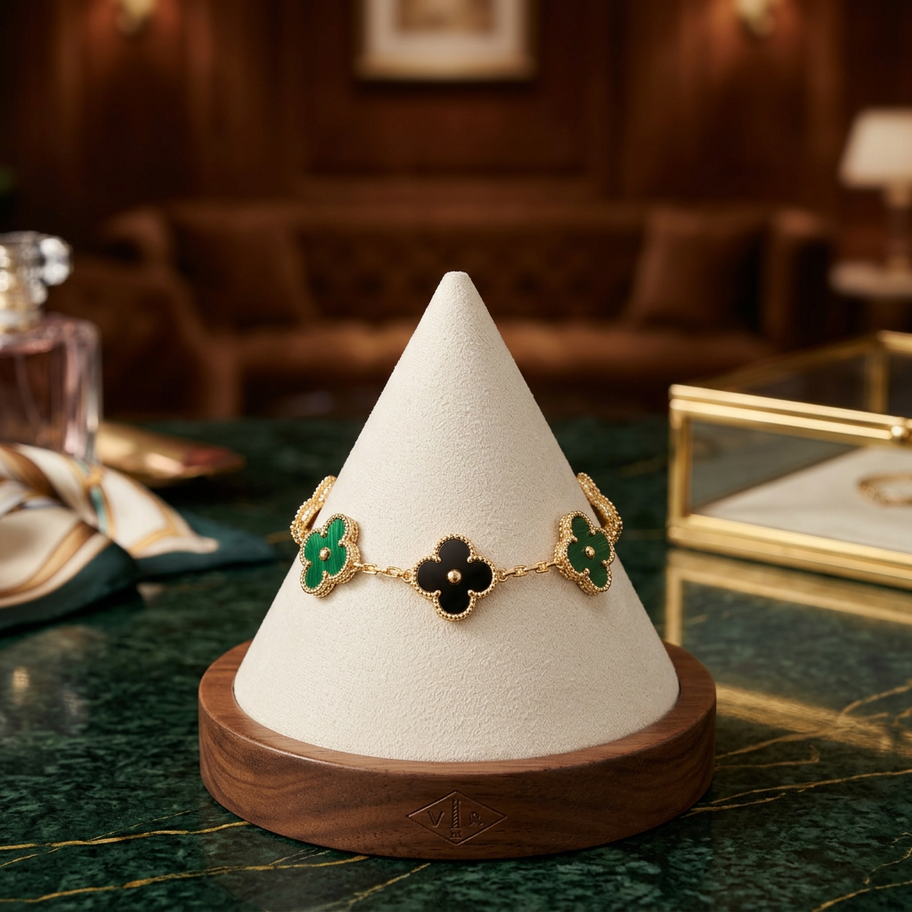 Gold bracelet with black and green clover charms on a white stand.