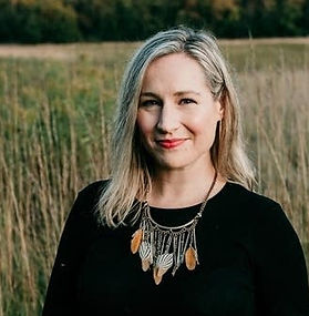 woman with blonde hair in black sweater with chunky necklace standing in a field of wheat