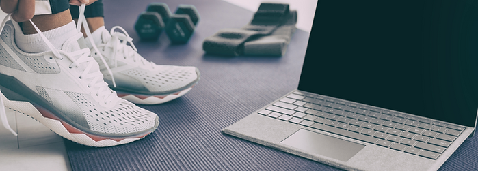 A pair of athletic shoes placed next to a laptop, symbolizing remote training and online fitness coaching.
