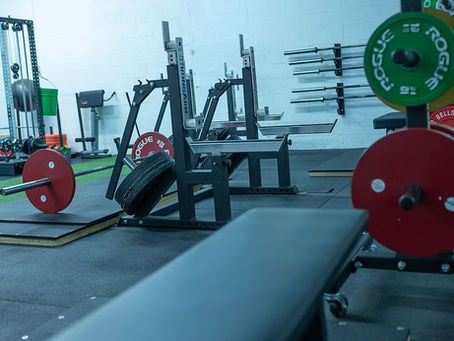 An interior picture of a gym showing racks, weight plates and a cable machine.