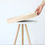Thumbnail: A white tray table with three legs and a round wood-trimmed table top that is being lifted off to use as a tray
