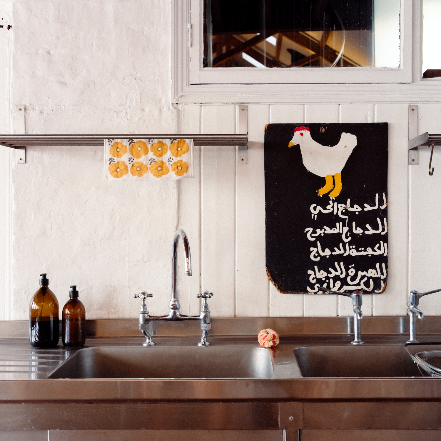 Rustic kitchen sink with painted chicken sign on the wall and a yellow flower motif Harada Orimono Kaya Kiji dishcloth hanging above the tap.
