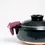 Thumbnail: A grape purple, semicircle Ban Inoue open oven mitt balanced on the handle of a brown, Japanese lidded hotpot bowl.