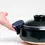 Thumbnail: A navy blue semicircle Ban Inoue pot holder oven mitt being used to hold the side of a large brown Japanese nabe bowl. The pot holder is an open mitt, made from a lightly padded muslin and features a braided cord for hanging.