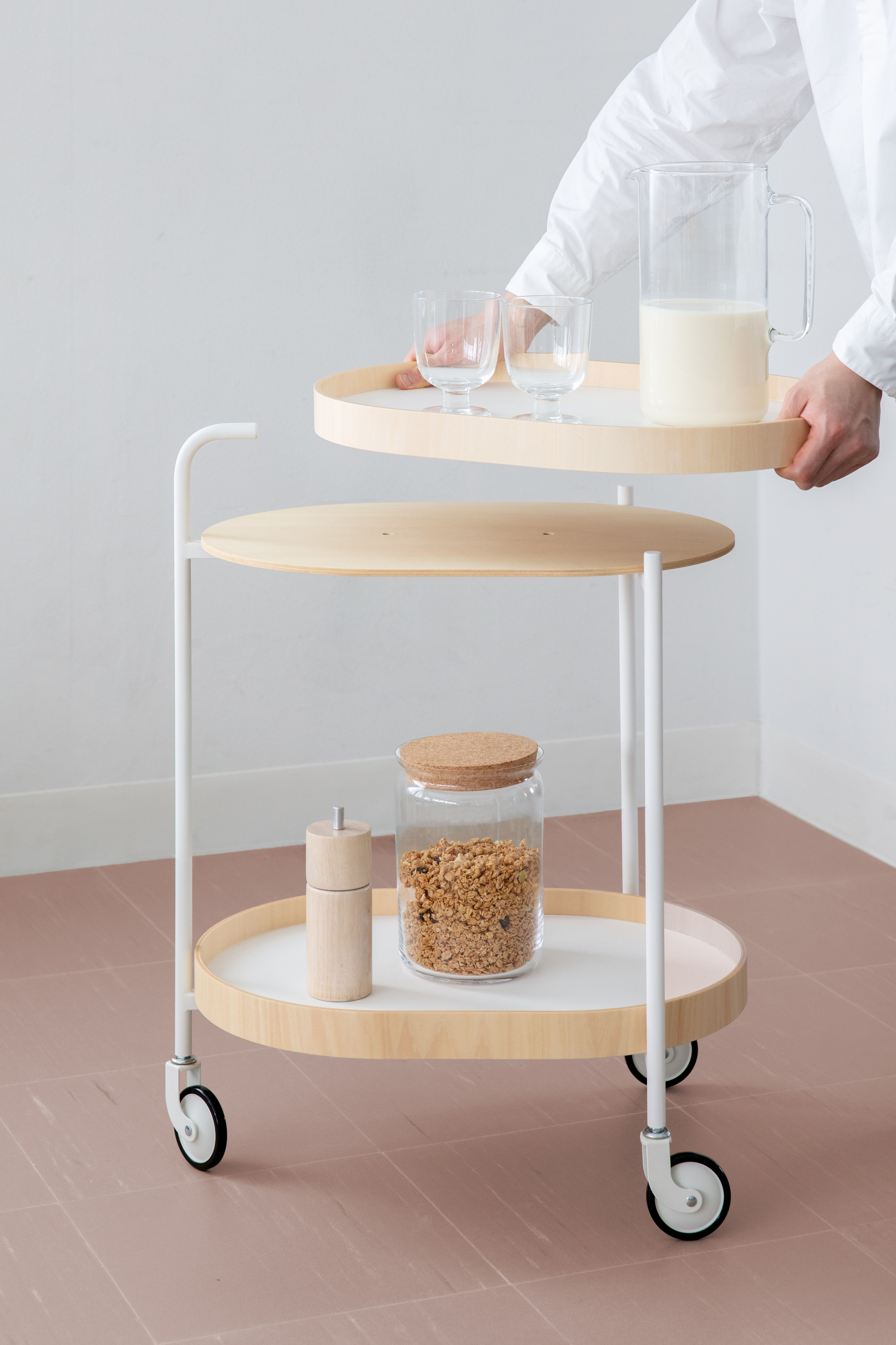 An oval shaped 2-tier drinks trolley with white frame and wood-trimmed white table tops, which can be removed as trays
