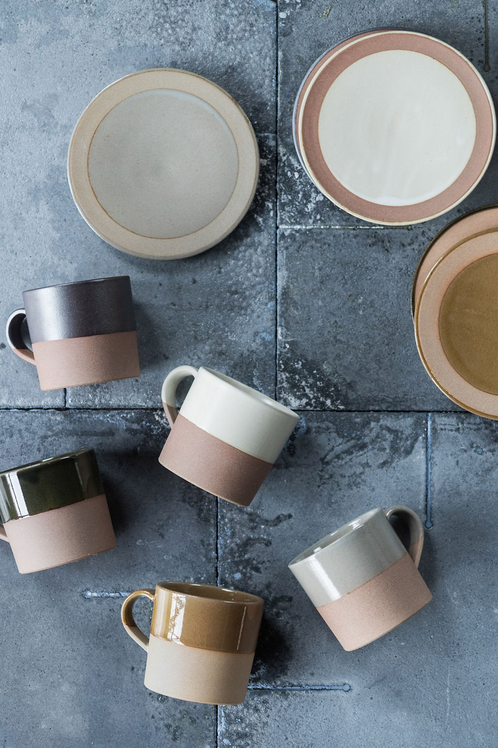 Thumbnail: A top view of 4 earthy-toned coffee cups and saucers designed by Angle in Japan. Each mug is dip glazed to the handle in either brown, taupe, grey or white. The centres of the saucers are glazed in matching colours.