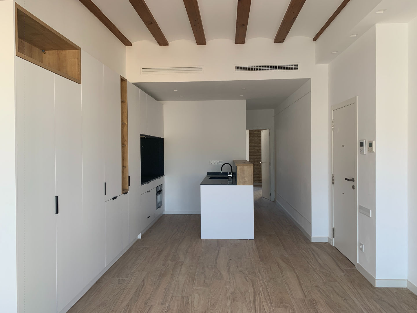 Espacio abierto con cocina isla y vigas vistas en vivienda unifamiliar reformada por Genovés Calleja Arquitectos.