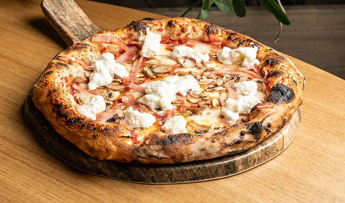 An authentic Neapolitan pizza topped with ham, fresh mushrooms, and creamy stracciatella cheese at Lucca Trattoria, a premium Italian restaurant offering Modern Italian Food and Neapolitan Pizzas in Doral Miami.