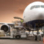"Avión de carga siendo cargado con cajas tipo courier mediante banda mecánica en pista de aeropuerto, supervisado por trabajadores con chalecos de seguridad bajo cielo parcialmente nublado.