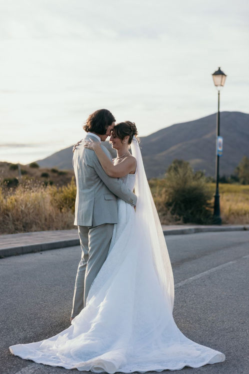 Novios abrazados al atardecer en Mijas durante su sesión de boda, con paisaje de montaña y luz cálida mediterránea.