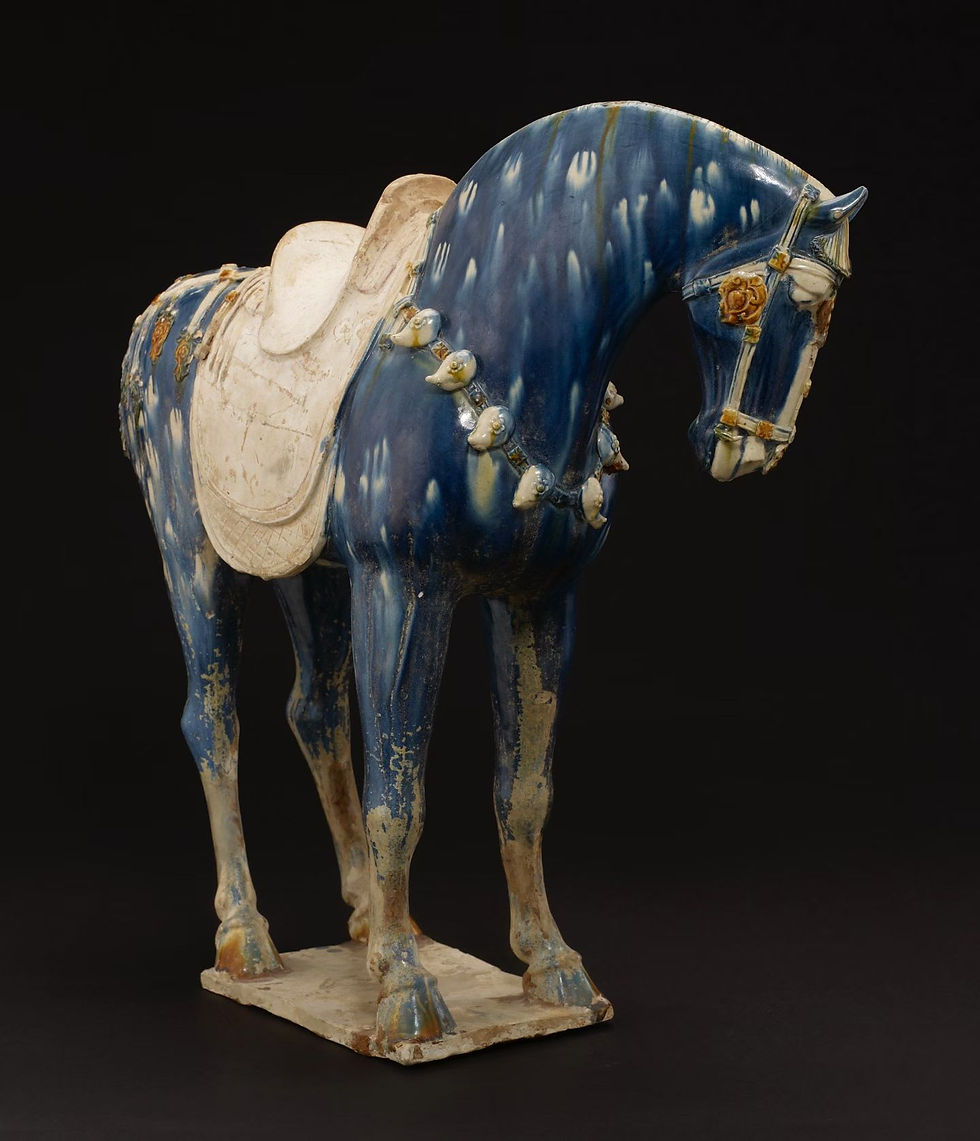 Blue ceramic horse sculpture with a white saddle adorned with beaded harness. Set against a dark background, exuding a serene elegance.