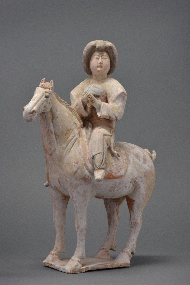 加彩騎馬婦人俑 Painted Pottery Figurine of Woman / Clay figurine of a person in traditional attire riding a horse. The figure is serene, holding an object. Gray background, neutral tones.