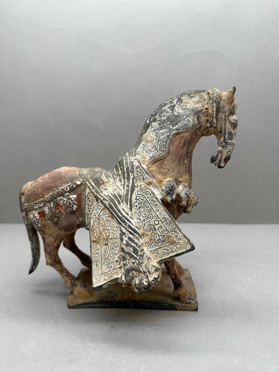 北魏陶加彩馬俑,平野古陶軒 A decorative terracotta horse figurine with intricate patterns and muted colors, standing against a plain gray background.