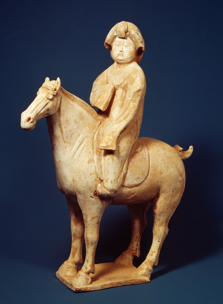 加彩騎馬婦人俑 Painted Pottery Figurine of Woman Terracotta figurine of a rider on a horse, wearing a hat, against a dark blue background. The statue is beige with a serene expression.