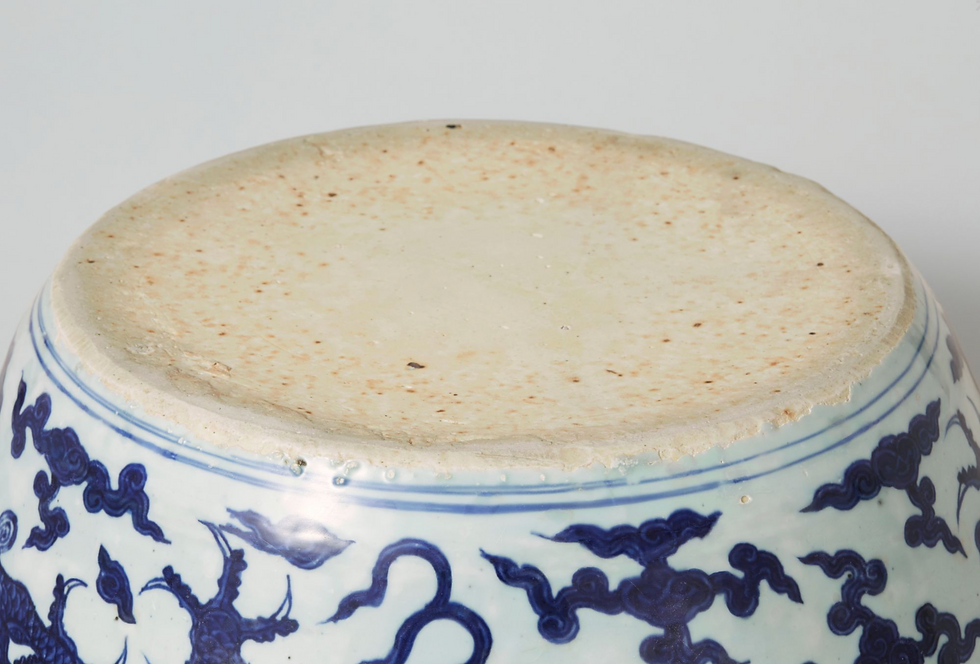 Close-up of the base of a ceramic bowl with blue dragon patterns on white background, showing a slightly textured and distressed edge.