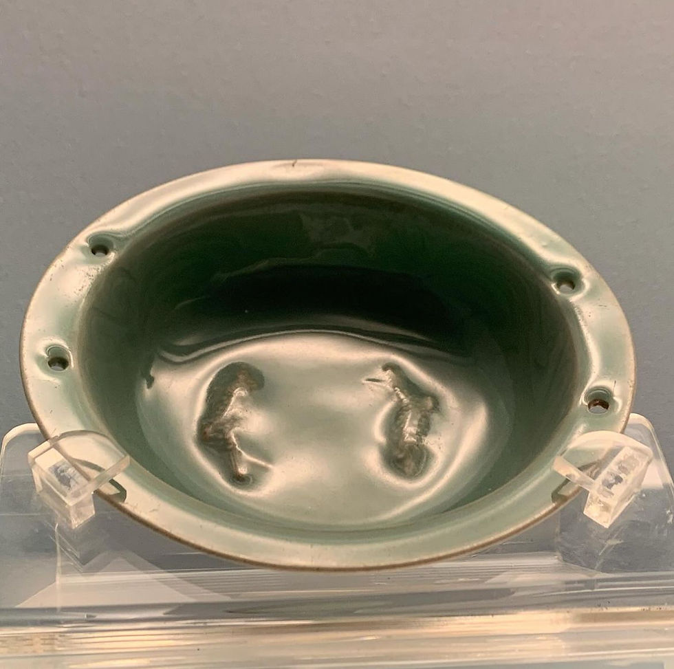 Green ceramic bowl with etched seahorses, displayed on a clear stand against a neutral background. Subtle shine on the smooth surface.