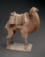 Ancient clay camel figurine with saddle packs, standing on a base against a dark studio background.