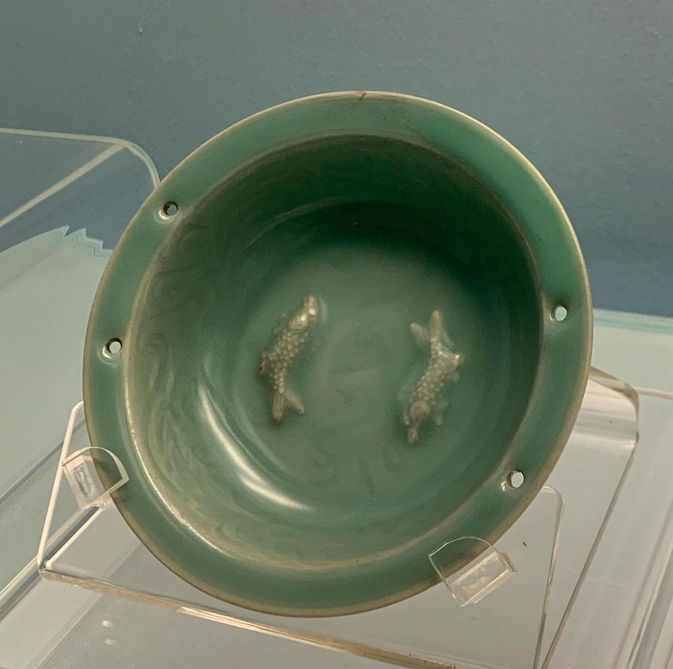 Green ceramic bowl with two raised fish designs inside. The bowl is displayed on a clear stand against a blue background.