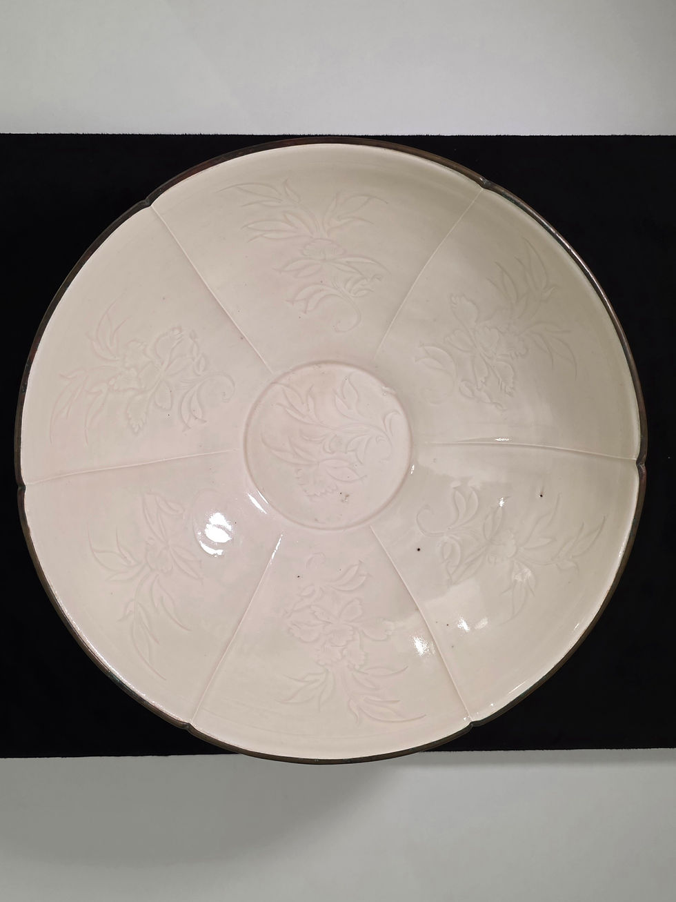 Large off-white ceramic plate with embossed floral patterns, shown against a black-and-white background.