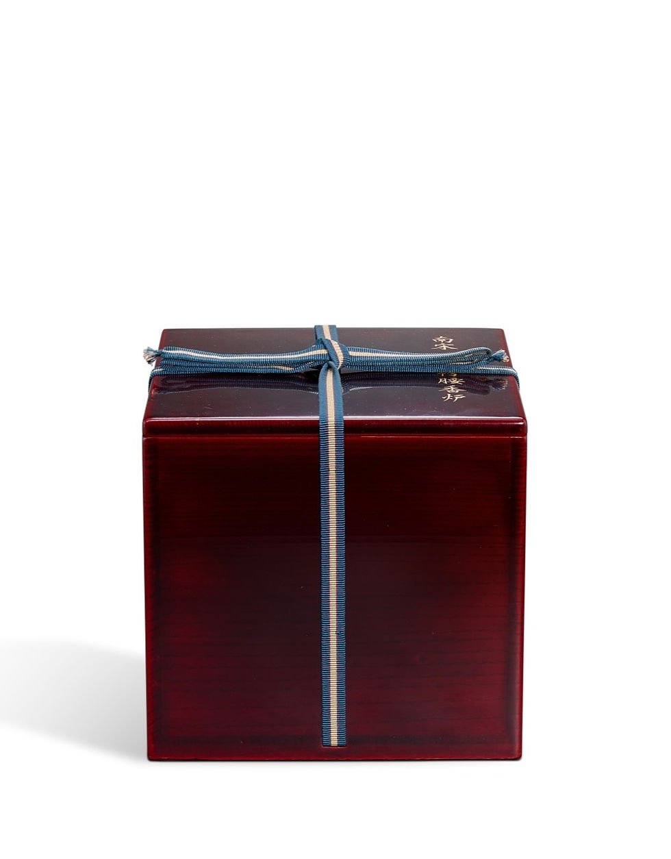 蘇富比伊勢彥信專場:南宋龍泉青釉鬲式爐 Red wooden box tied with a blue ribbon, featuring gold text on the lid. The box is set on a plain white background.