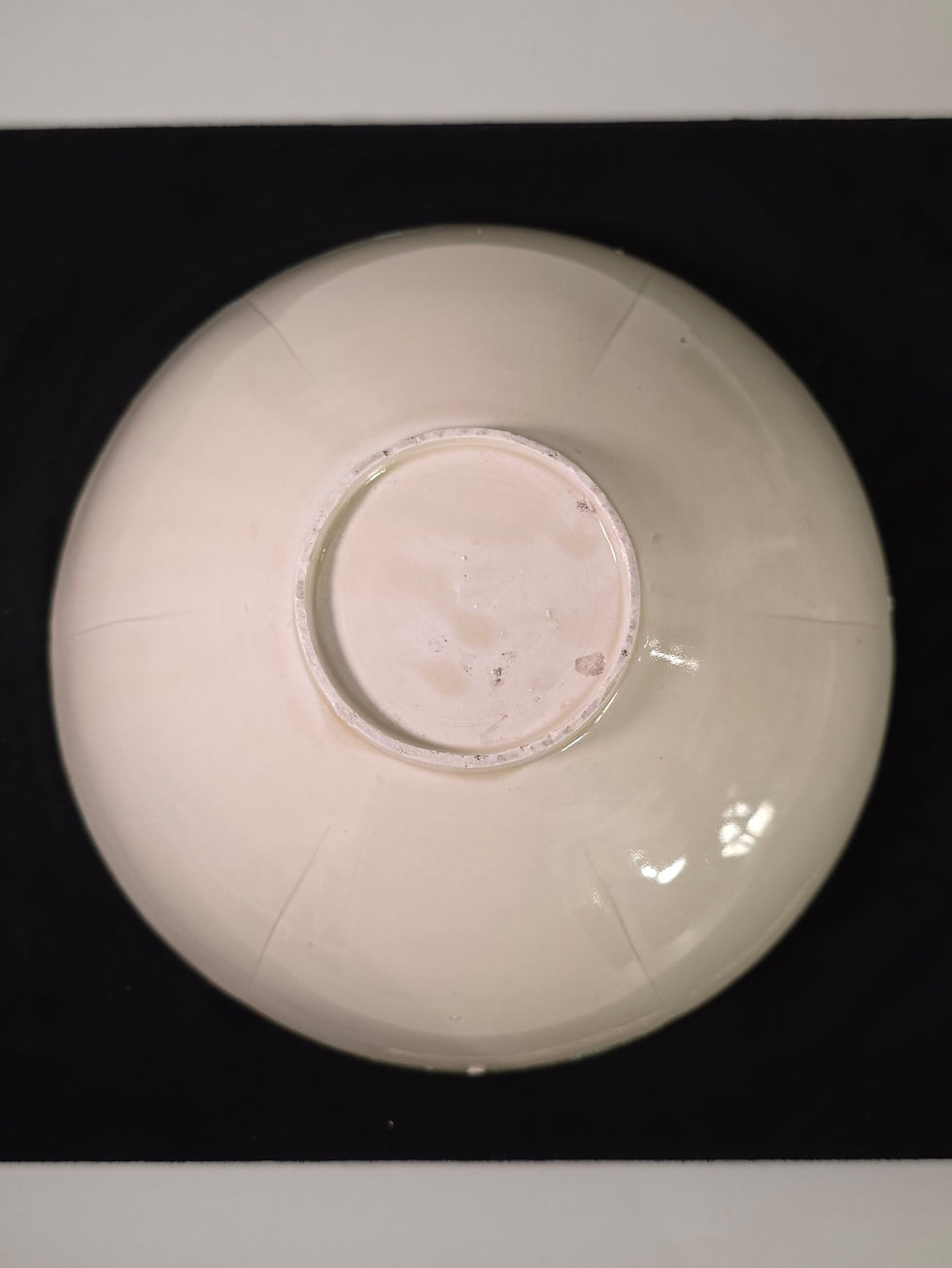 Upside-down white bowl centered on a black background, with faint scuffs and reflections.