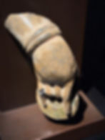 Stone hand sculpture with pointing finger on a dark background. The surface is textured with earthy tones, displayed under focused lighting.