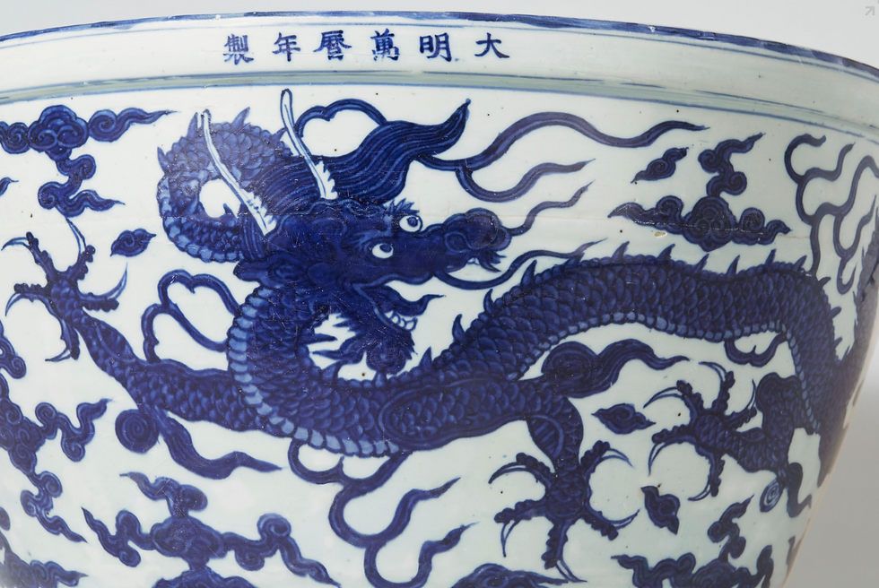 Blue dragon design on a white porcelain bowl with Chinese characters along the rim. The dragon is surrounded by stylized clouds.