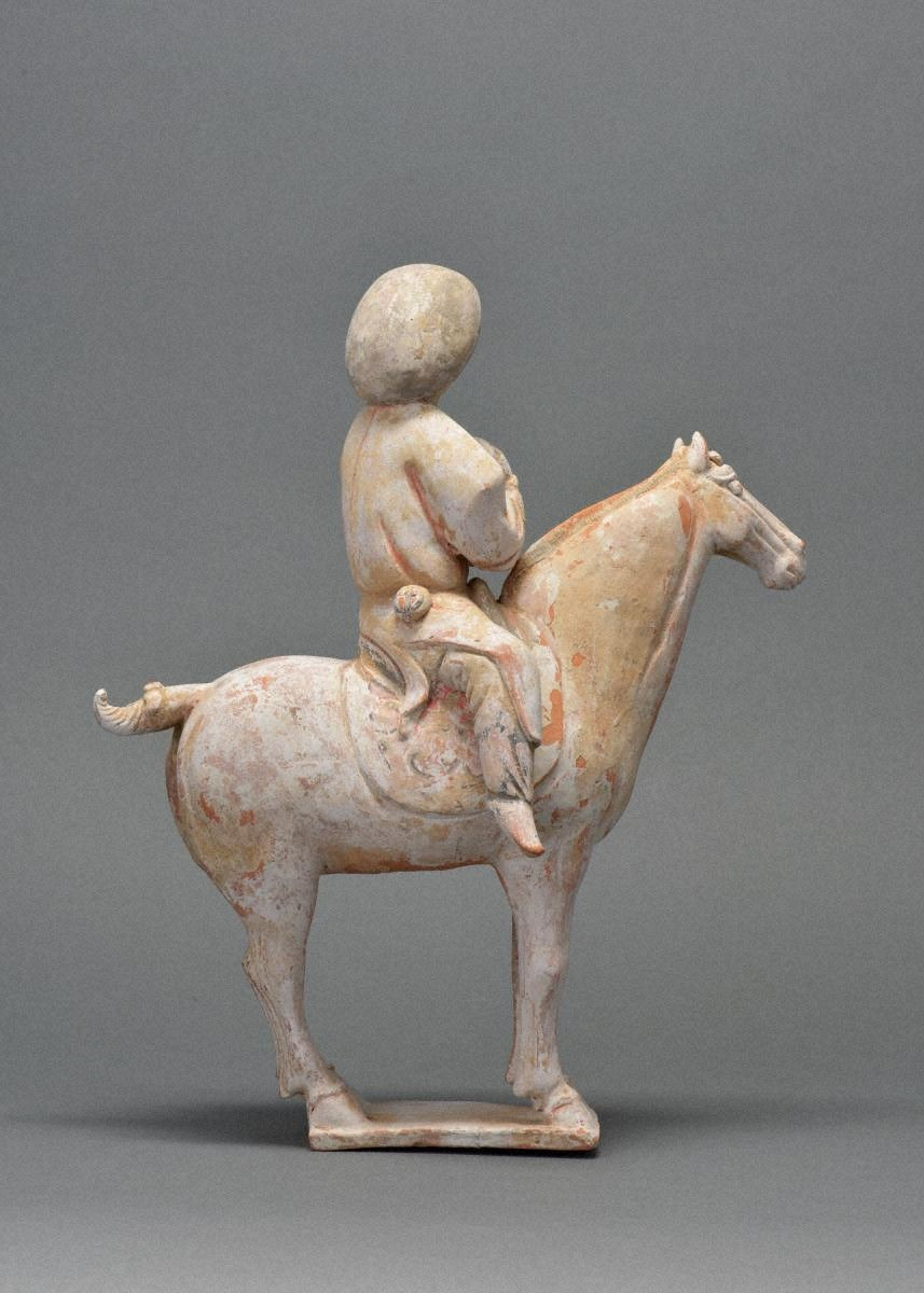 加彩騎馬婦人俑 Painted Pottery Figurine of Woman / Ancient clay figurine of a person riding a horse. The sculpture is in muted earth tones and set against a plain gray background.
