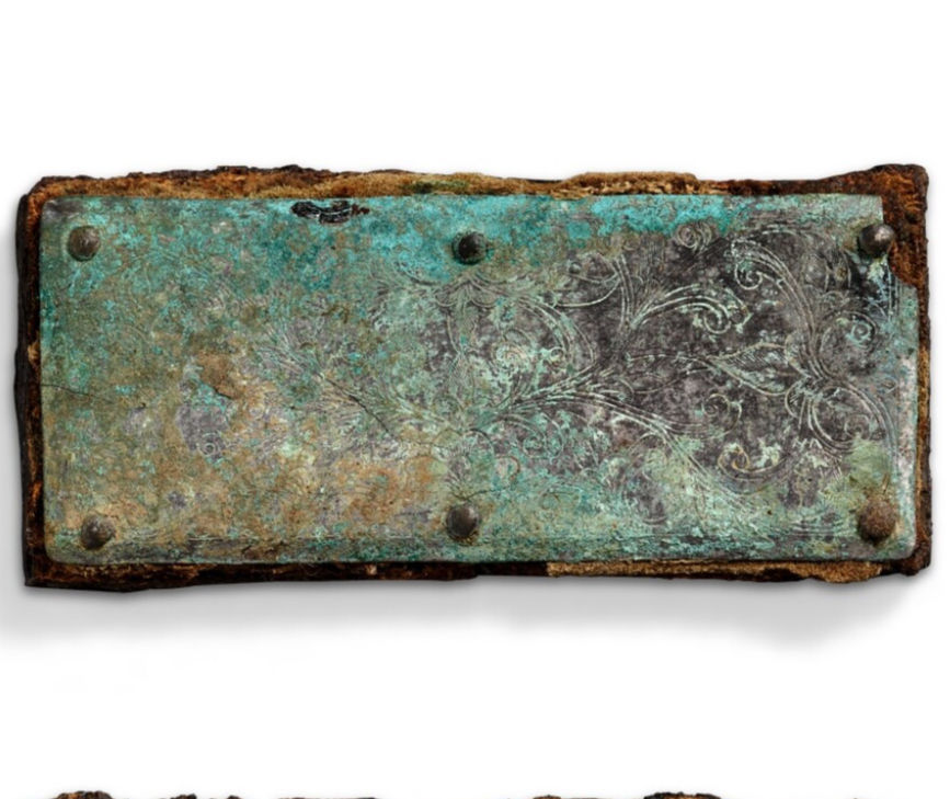 Antique metallic plaque with intricate, engraved floral patterns, heavily oxidized with green and brown hues, secured with four bolts.