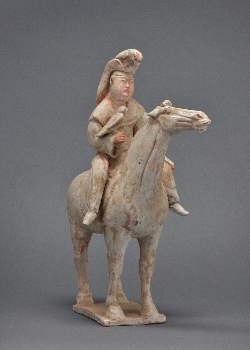 加彩騎馬婦人俑 Painted Pottery Figurine of Woman / Ancient terracotta figurine of a person riding a horse, holding a bird. The statue is in earthy tones against a plain gray background.
