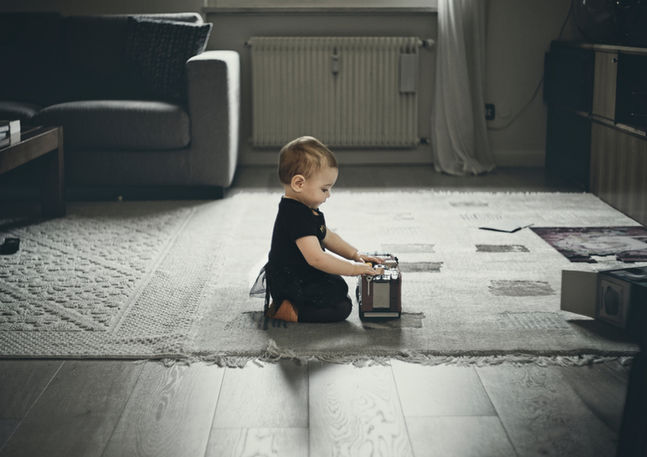 A toddler sits on the floor playing with a toy miniature bus. Image (c) Lenny Di Lorenzo.