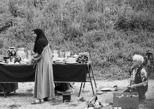 A man is kneeling in front of a Muslim woman looking at ceramics at a street market. Image (c) Lenny Di Lorenzo.