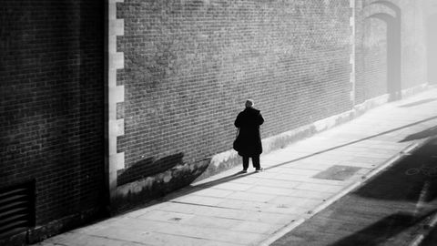 Man stands on sidewalk in front of a tall brick wall. Image (c) Lenny Di Lorenzo.