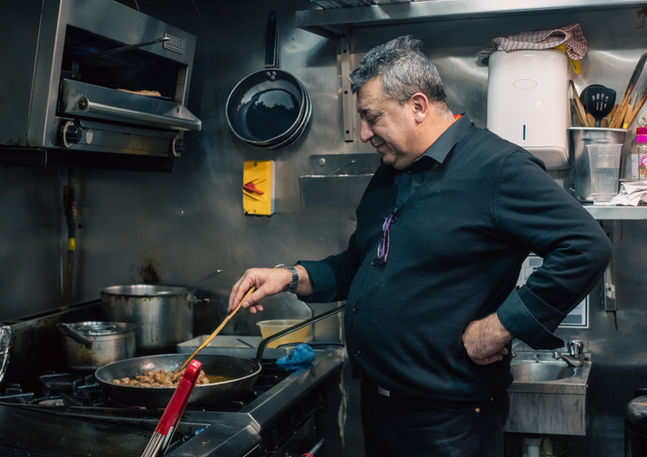 A middle age Kurdish man is cooking in his kitchen. Image (c) Lenny Di Lorenzo.