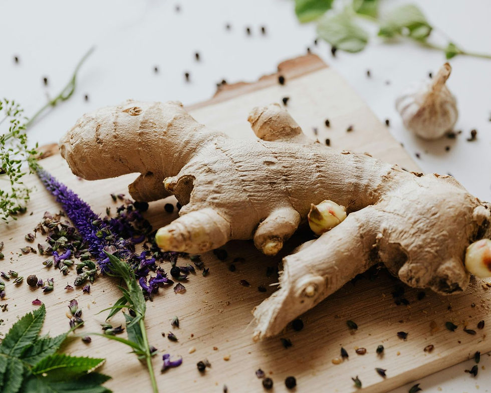 A ginger root on a wooden board with scattered purple flowers, green leaves, and peppercorns, creating a rustic and natural vibe.