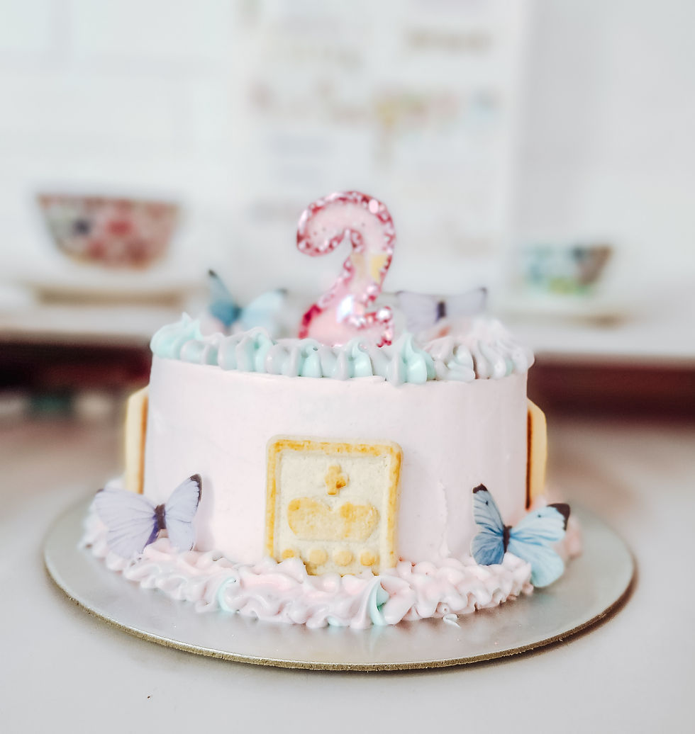 Pink birthday cake with a glittery number 2 topper, pastel swirls, and butterfly decorations. Cookies adorn the side. Soft background.