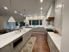 large kitchen renovation with double sinks and oven with range hood white countertops and kitchen island with built in sink and microwave