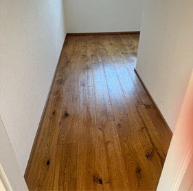Professionell verklebter Fertigparkettboden mit geölter Oberfläche und exakt verlegten Sockelleisten