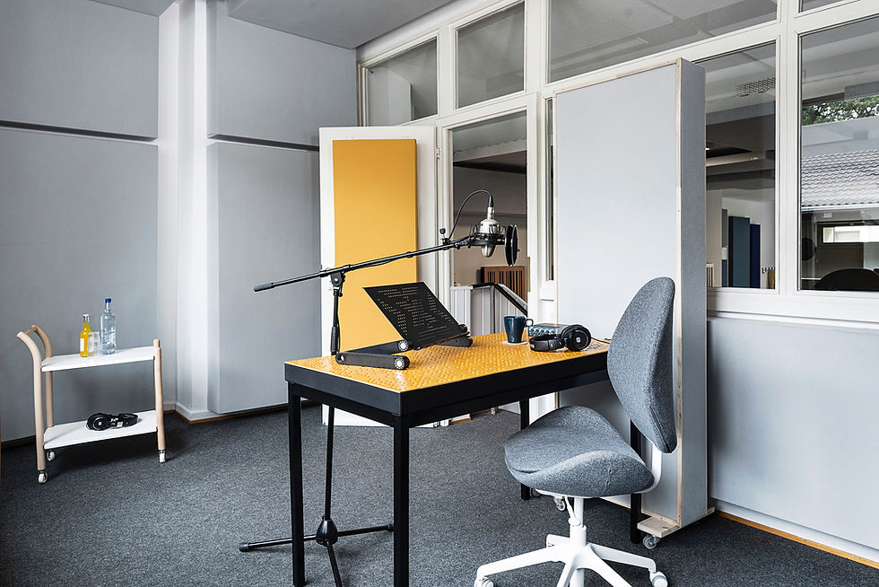 Moderner Sprecherplatz im Tageslicht-Studio mit Mikrofon, Notenständer und bequemem Arbeitsstuhl. Die offene Glasarchitektur sorgt für eine helle und freundliche Atmosphäre während der Produktion.