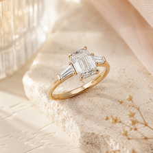 Angled view of an emerald cut diamond engagement ring with tapered baguette side diamonds in yellow gold.