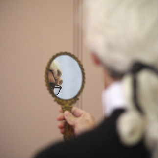 un visiteur perruqué se regarde dans le miroir doré
