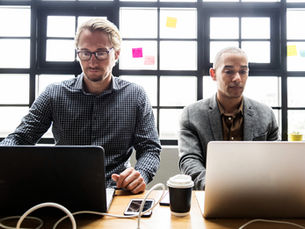 two people sitting at a table working on their laptops