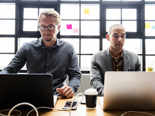 two people sitting at a table working on their laptops