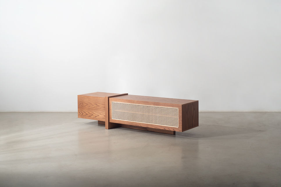 Lina Media Console in natural wood veneer with two offset volumes and a caned door panel, on a concrete floor