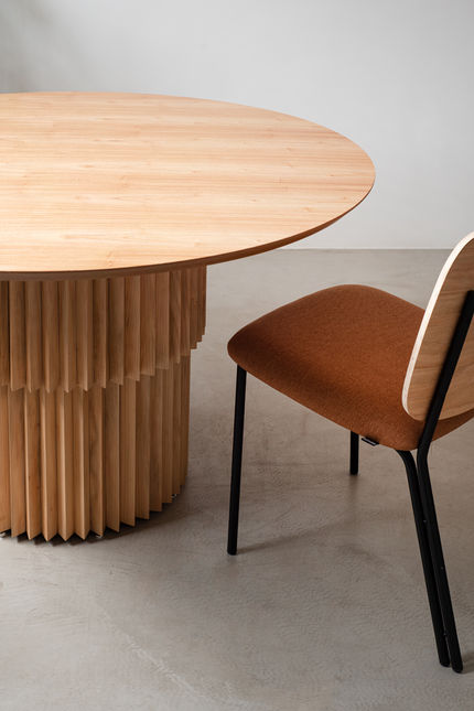 Madalena Chair with terracotta seat pulled up to a round wooden dining table with a fluted pedestal base