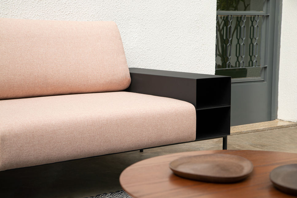 The steel niche arm of the Marcelo Sofa seen beside the blush pink seat and a round wooden coffee table