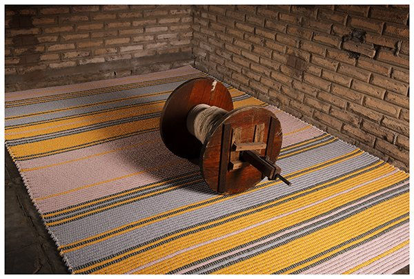 Handwoven Taboa fibre rug with yellow, grey and pink stripes, laid out with a wooden warp beam on top