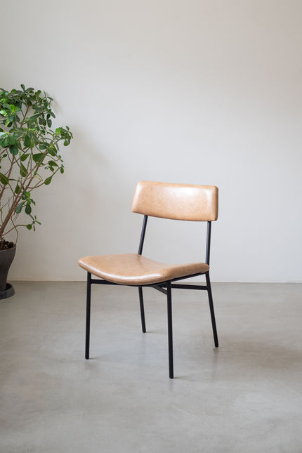Luiza Chair with a black carbon steel frame and tan upholstered seat and backrest, beside a potted plant
