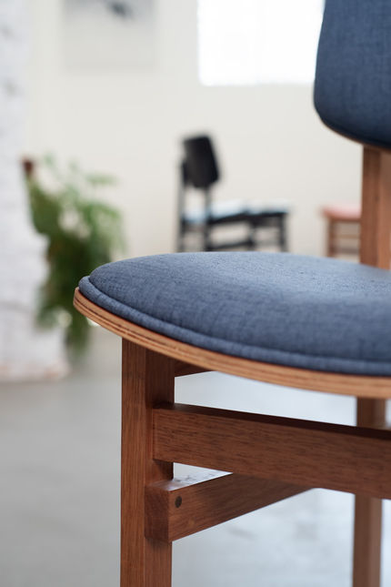 Joseph Chair with a blue seat seen up close in a studio, with other chairs from the family out of focus behind